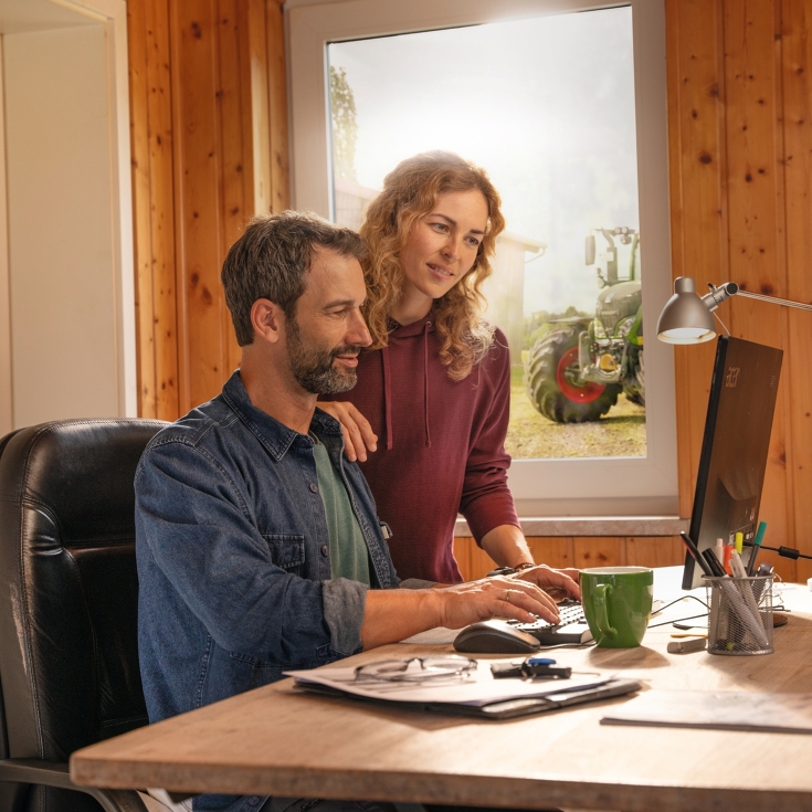 Um casal de agricultores na frente de seu computador, no escritório, criando limites de campo com a agronomia FendtONE