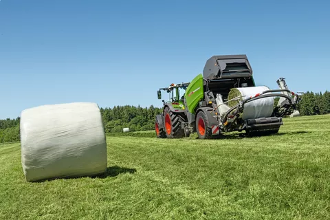 Fendt Traktor zieht Fendt Rotana 130F Rundballenpresse über Wiese mit foliengebundenen Heuballen