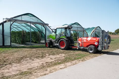 Ein Fendt e100 V Vario fährt in einen Obsttunnel mit Himbeerpflanzen