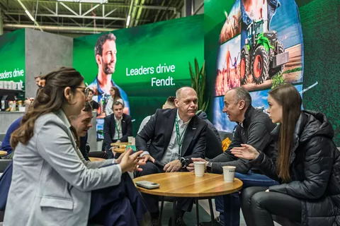 Mehrere Personen sitzen um einen Tisch und unterhalten sich, im Hintergrund weitere Messebesucher