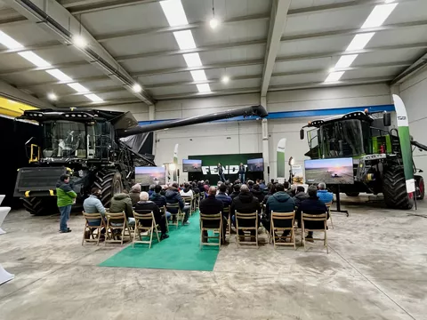 Landwirte sitzen in einer Halle auf Stühlen mit Blick auf eine Bühne; links steht ein Fendt IDEAL Mähdrescher in anthrazit und rechts ein Fendt Schüttlermähdrescher in grün, der Fotograf stand im Rücken der sitzenden Landwirte