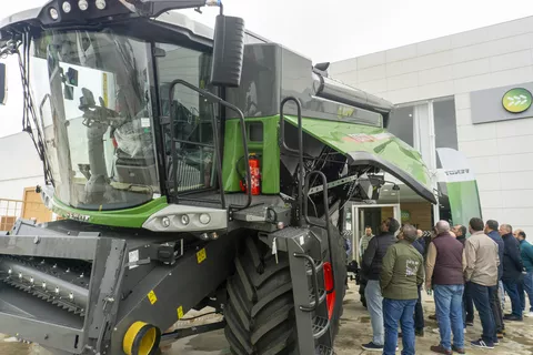 Eine Gruppe von Landwirte schaut unter das aufgeklappte Seitenteil eines Fendt Schüttlermähdreschers 6335 C PLI vor einer Halle