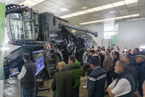Eine Gruppe von Landwirte schaut unter das aufgeklappte Seitenteil eines Fendt Fendt IDEAL 7 PL Rotor-Mähdreschers in einer Halle