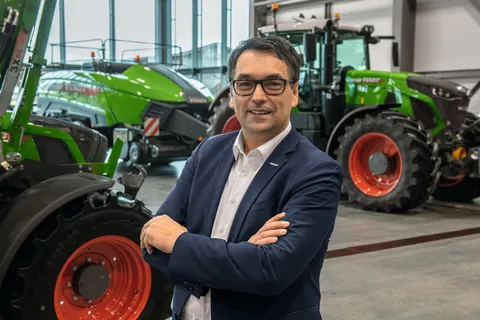 Roland Schmidt, Vice President Fendt Marketing in einer Halle, im Hintergrund grüne Fendt Traktoren und eine Quaderballenpresse