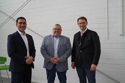 3 Männer lächeln gemeinsam in die Kamera und stehen vor einer weißen Wand