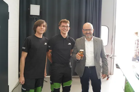 3 Männer, 2 davon sind Azubis (links), der Mann rechts trinkt ein gezapftes Kaltgetränk