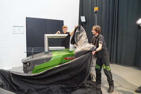 2 Azubis ziehen an einem schwarzen Tuch, darunter die Fendt Zapfanlage