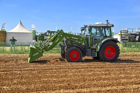 grüner Fendt e100 Vario mit Frontlader auf einem Feld im Hintergrund ein Zelt