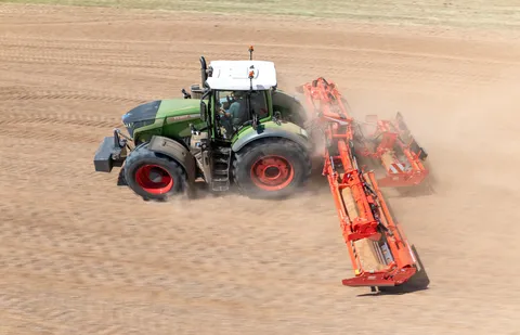 Grüner Fendt 1050 Vario Traktor mit Kreiselegge im Gespanne auf einem staubigen Feld