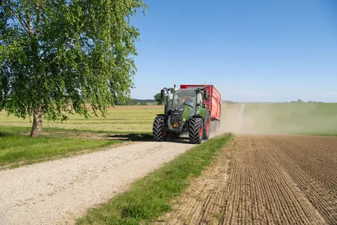 Ein grüner Fendt 300 Vario fährt mit einem roten Anhänger einen Feldweg hinauf.