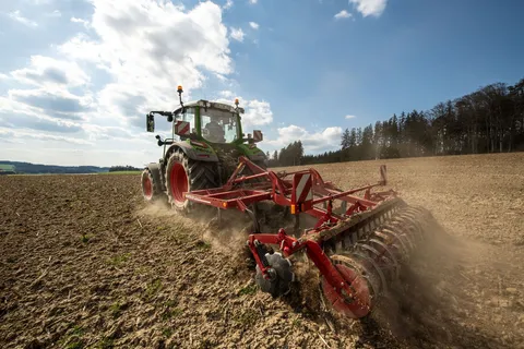 Ein grüner Fendt 300 Vario arbeitet mit einem Horsch Grubber auf dem Acker.