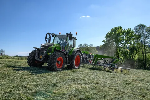 Ein grüner Fendt 500 Vario fährt mit einem Fendt Former Mittelschwader über eine gemähte Wiese und schwadet.