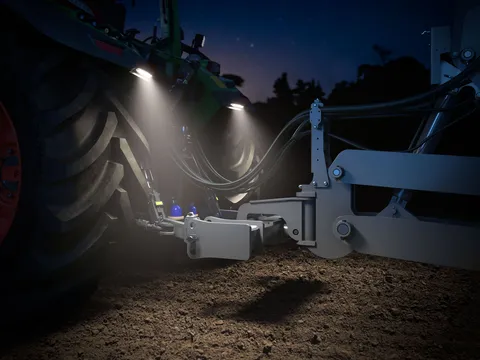 Ein Fendt 500 Vario im Dunklen fotografiert mit aktivierter GroundVision Beleuchtung am Heck. Der Lichtstrahl fällt auf die Deichsel und die Front des Anbaugerätes.
