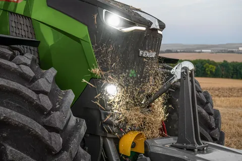 Die Front eines grünen Fendt 800 Vario Traktors mit eingeschalteten Leuchten mit Stroh vor dem Kühlergitter, dass vom Umkehrlüfter weggeblasen wird.