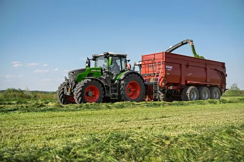 Eine grüner Fendt 800 Vario fährt neben einem Häcksler während dieser den roten Anhänger von Krampe füllt.