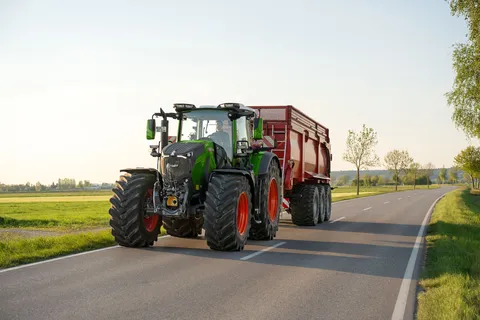 Ein grüner Fendt 800 Vario fährt mit einem roten Anhänger von Krampe über die Straße.