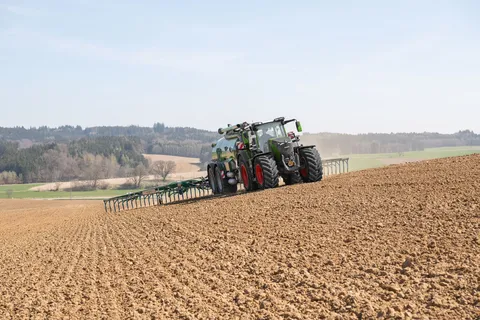 Der grüne Fendt 800 Vario fährt mit einem Güllefass über ein Feld und bringt Gülle aus.