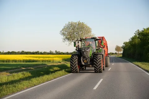 Ein grüner Fendt 800 Vario fährt mit einem roten Anhänger von Krampe über die Straße.