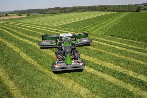Ein grüner Fendt 800 Vario wendet mit angehobenen Mähwerken auf dem Grünland.