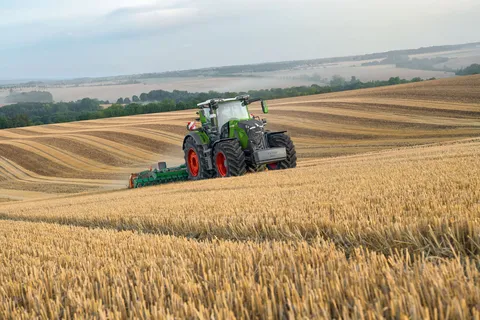 Ein grüner Fendt 800 Vario fährt im Gespann mit einer Scheibenegge von Amazone über ein Stoppelfeld, Im Hintergrund sind Äcker und Wald zu sehen.