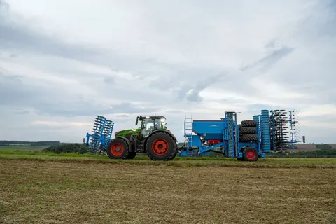 Ein grüner Fendt 800 Vario fährt im Gespann mit einem Frontpacker und einer blauen Einzelkorndrille von Lemken im Heck über einen Feldweg.