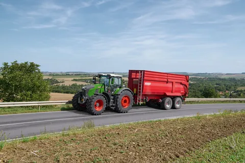 Ein grüner Fendt 800 Vario fährt mit einem roten Anhänger von Krampe über die Straße.