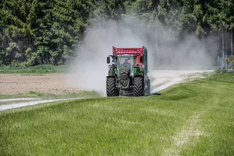 Ein grüner Fendt 724 Vario Gen7.1 fährt im Gespann mit einem Strautmann Ladewagen über einen Feldweg direkt auf die Kamera zu. Im Hintergrund ist ein Wald zu sehen.