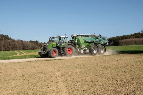 Ein grüner Fendt 724 Vario Gen7.1 fährt mit einem Güllefass über einen Feldweg.