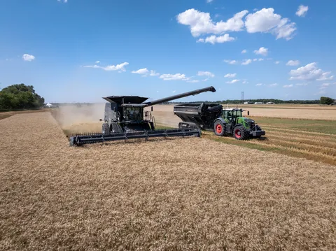 Ein schwarzen Fendt IDEAL tankt in einen schwarzen Überladewagen ab, der von einem autonom fahrenden grünen Fendt Traktor gezogen wird