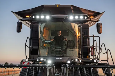 Ansicht auf einen schwarzen Fendt IDEAL Mähdrescher bei der Ernte im Getreidefeld mit eingeschalteten Scheinwerfern