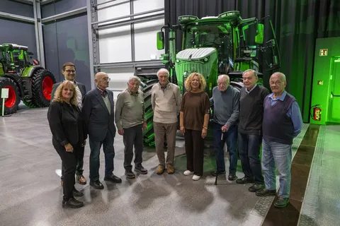 Eine Gruppe von Menschen steht vor einem grünen Traktor in einem Ausstellungsraum.