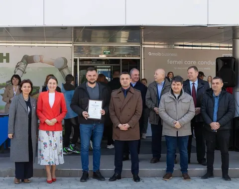 Eine Gruppe von Menschen steht vor einem Gebäude; ein Mann hält eine Urkunde in der Hand.