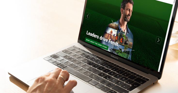 Eine Person sitzt an einem Laptop. Von der Person sieht man nur einen kleinen Teil des Handrücken. Der Laptop ist aufgeklappt und zeigt eine Website.