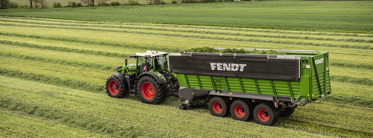 Fendt 900 Vario mit Fendt Tigo XR Ladewagen beim Aufsammeln schon Grasschwaden auf einer Wiese.