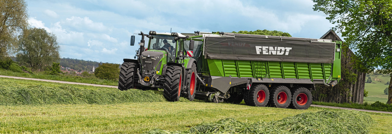 Fendt Tigo Ladewagen mit einem Fendt 900 Vario Traktor beim Laden von Gras auf einer Wiese.
