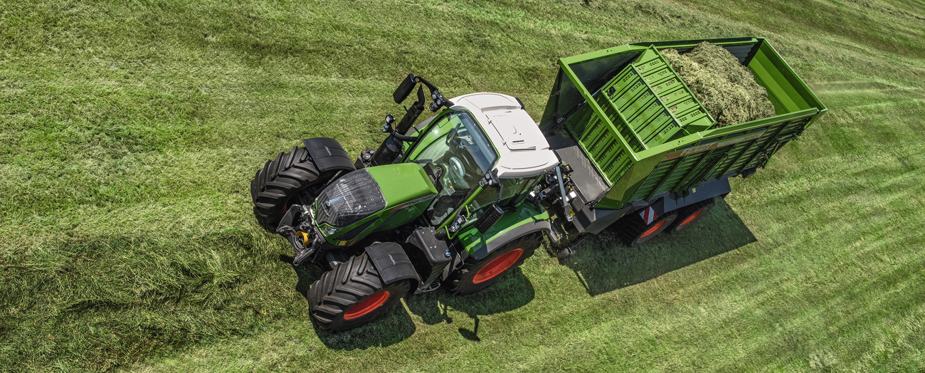 Luftaufnahme von einem Fendt 700 Vario mit Fendt Tigo Tandemladewagen auf einer Wiese.