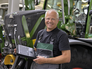 Fendt Mitarbeiter steht vor Schlepper mit Laptop in der Hand