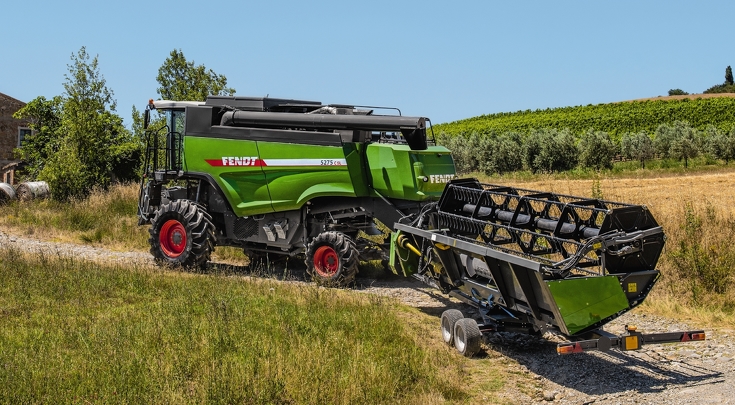 Der Mähdrescher 5275 C SL transportiert ein Schneidewerk auf einem Weg zwischen zwei Feldern.