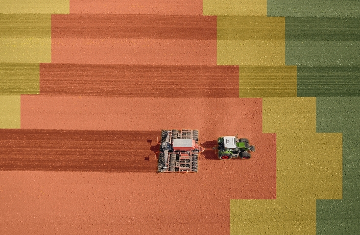 Ein Fendt Vario mit Drillkombination fährt über ein Feld, welches in gelbe, rote und grüne Flächen unterteilt ist.
