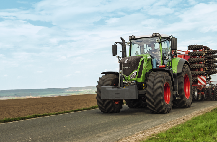 Fendt 800 Vario fährt mit Drillmaschine über eine Straße zwischen den Feldern.