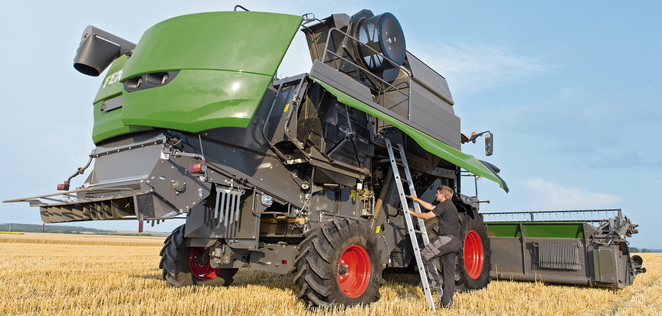 Ein Mann steigt an einer Treppe auf seinen Fendt Mähdrescher der C-Serie, welcher in einem Feld steht.