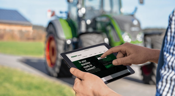 Mann steht vor dem Schlepper mit einem Tablet in der Hand auf dem Fendt Connect geöffnet ist.