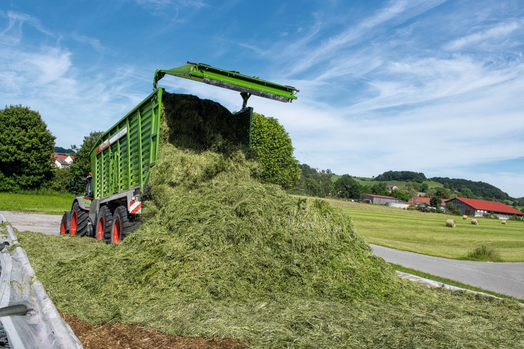 Fendt Tigo bei der Entladung des Grases im Silo mit Rundballen auf dem Feld im Hintergrund