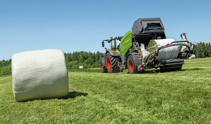 Fendt Traktor zieht Fendt Rotana 130F Rundballenpresse über Wiese mit foliengebundenen Heuballen