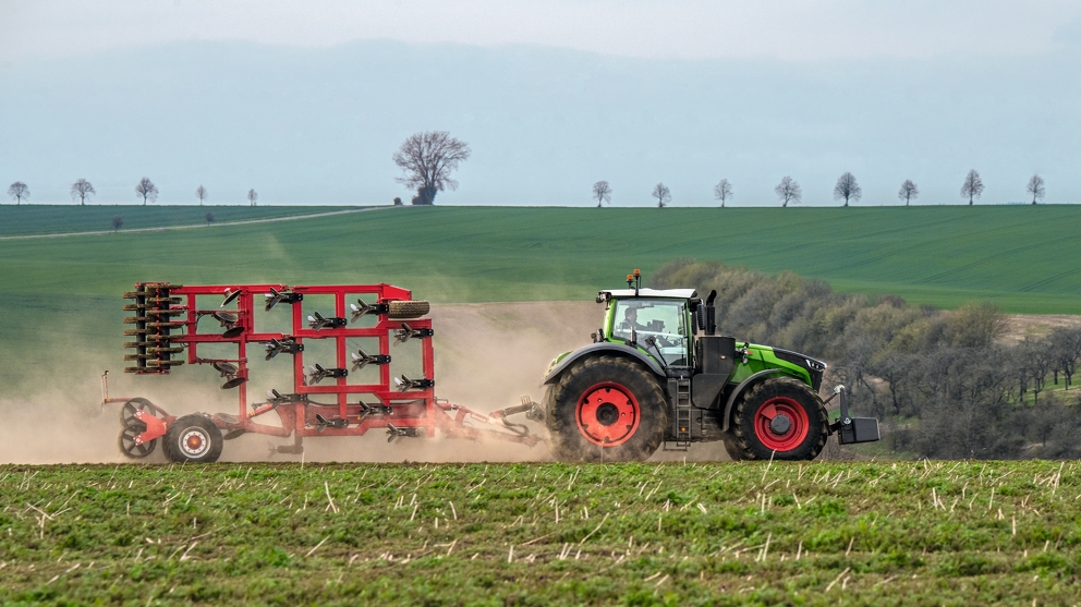 Seitenansicht des Fendt 1000 Vario mit eingeklappten Anbaugerät auf einem Feld