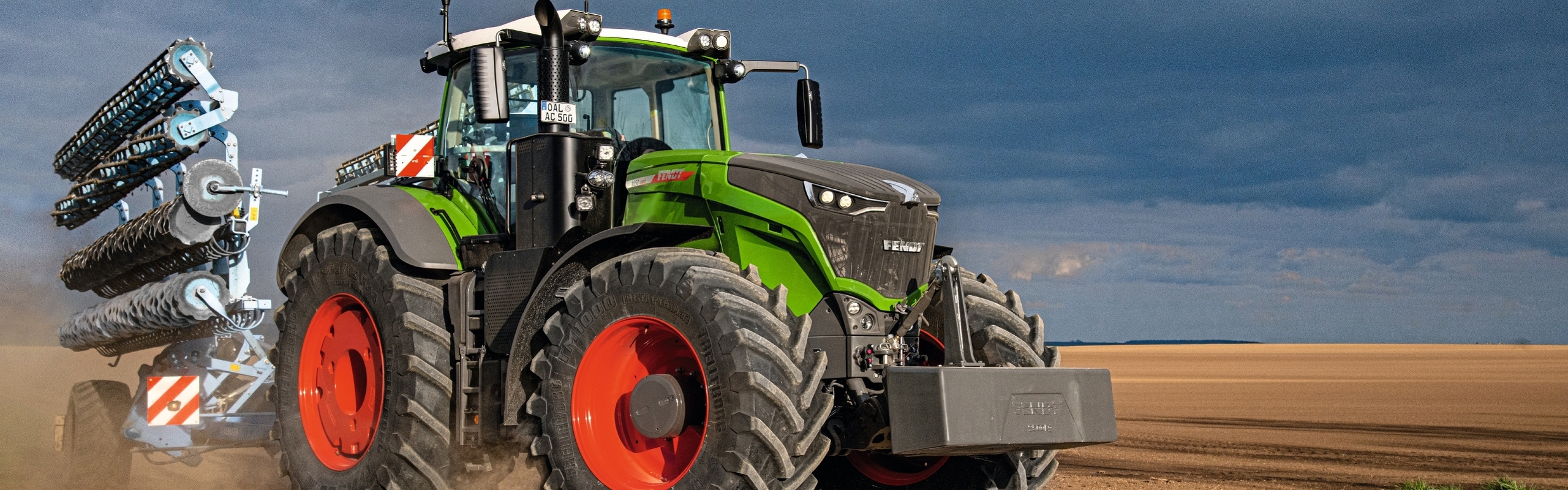 Ein Fendt 1000 Vario Traktor steht auf einem hellbrauen Acker mit Wolken im Hintergrund.