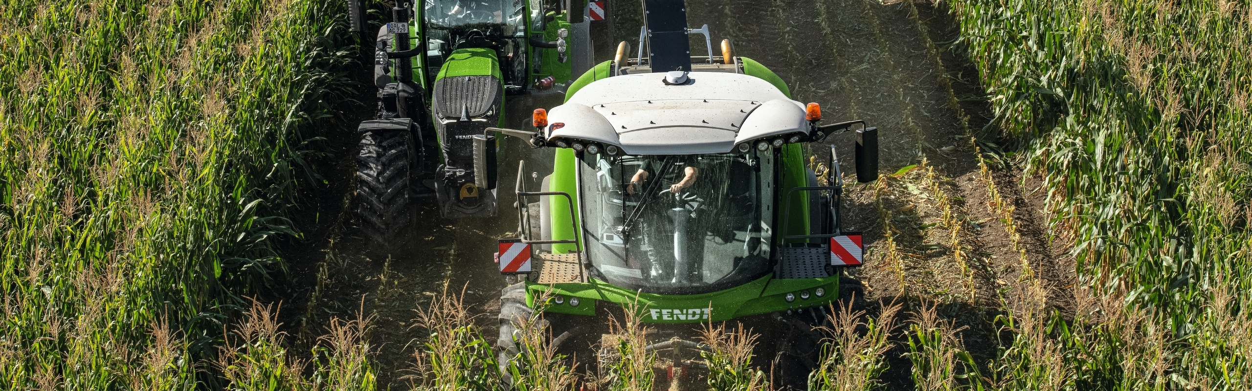 Fendt Katana neben einem Fendt Traktor auf einem Maisfeld aus der Vogelperspektive