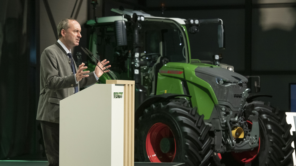 Ein Mann hält einen Vortrag vor Publikum. Im Hintergrund steht ein Fendt Traktor