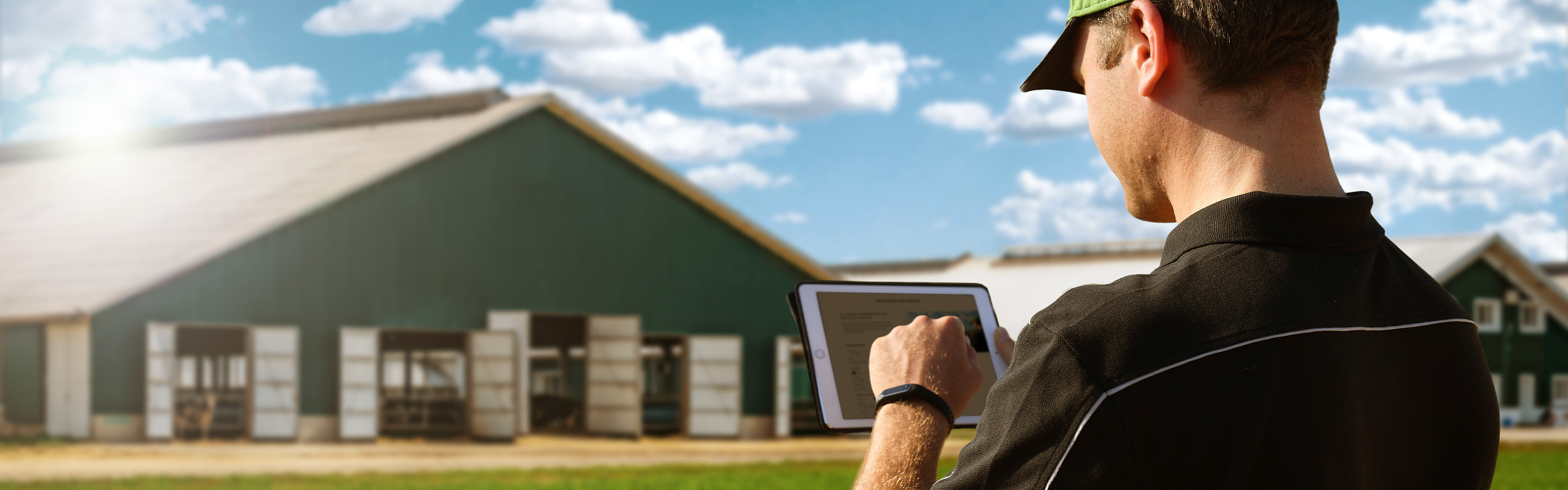 Ein Landwirt mit Tablet steht vor seinem Hof und meldet sich für den Newsletter an