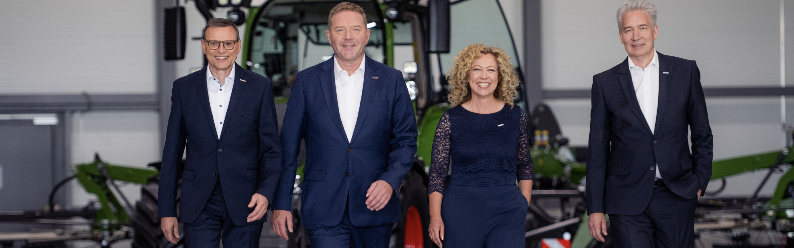 Walter Wagner, Christoph Gröblinghoff, Ingrid Bußjäger-Martin und Ekkehart Gläser stehen nebeneinander im Fendt Forum vor einem Fendt Traktor und lächeln.